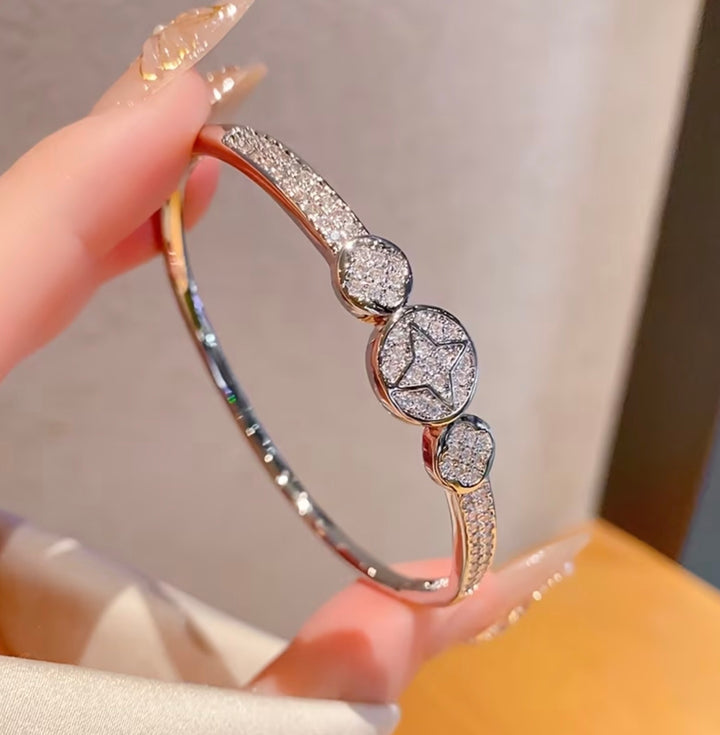 Silver crystal bangle bracelet with sparkling star and heart detail design on a silver-tone hinged cuff bracelet.