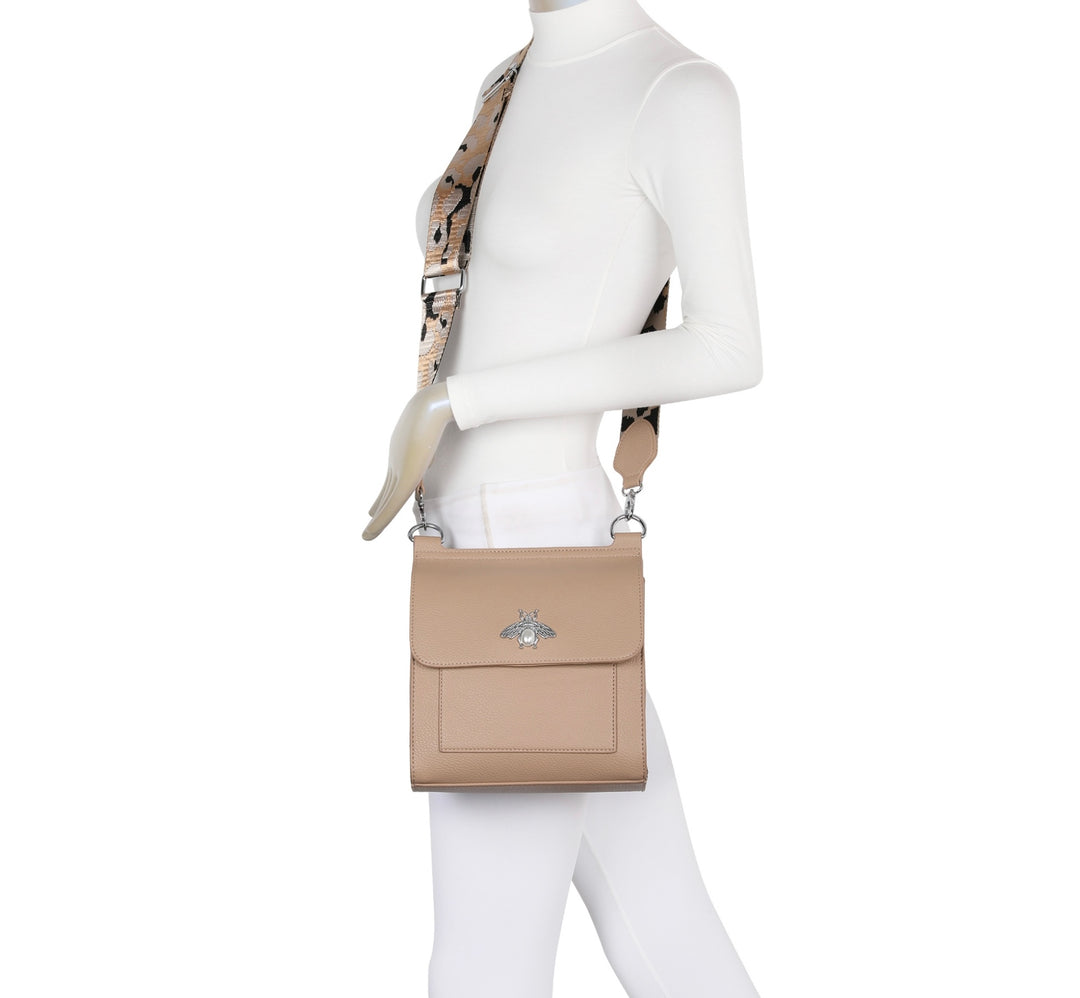 A beige satchel crossbody bag with a bee design on the front flap, featuring a camouflage pattern on the strap.