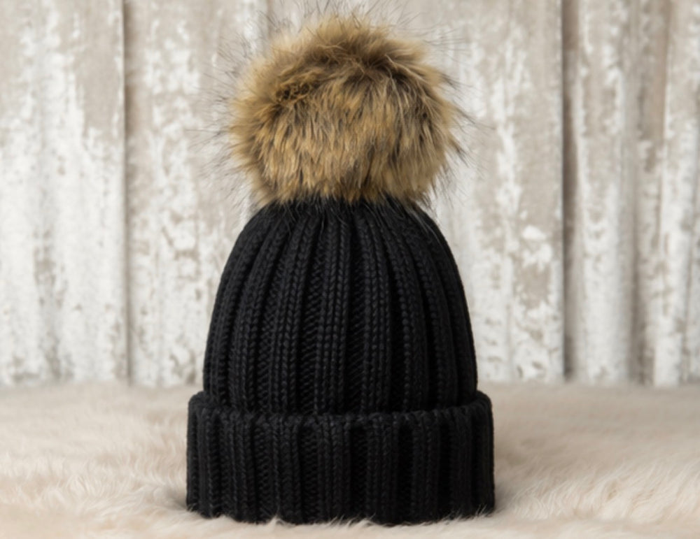 Children’s black ribbed knit bobble hat with a large beige faux fur pom pom