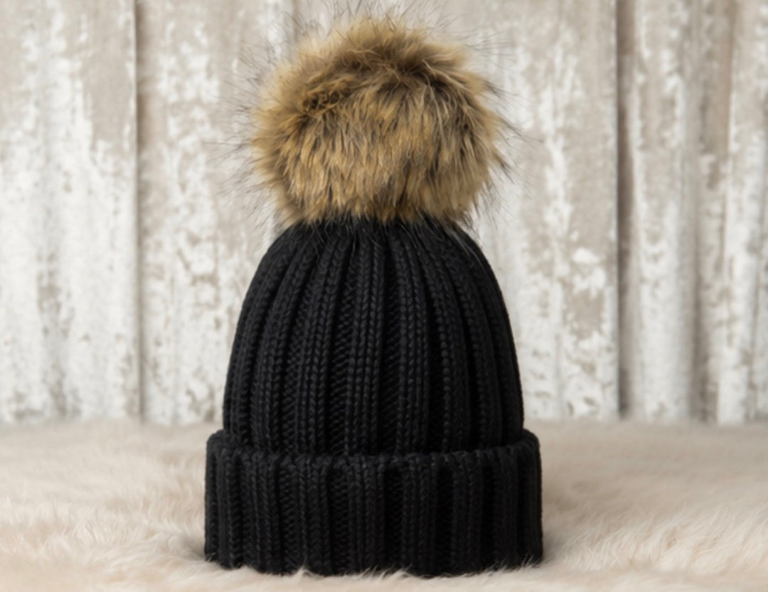 Children’s black ribbed knit bobble hat with a large beige faux fur pom pom