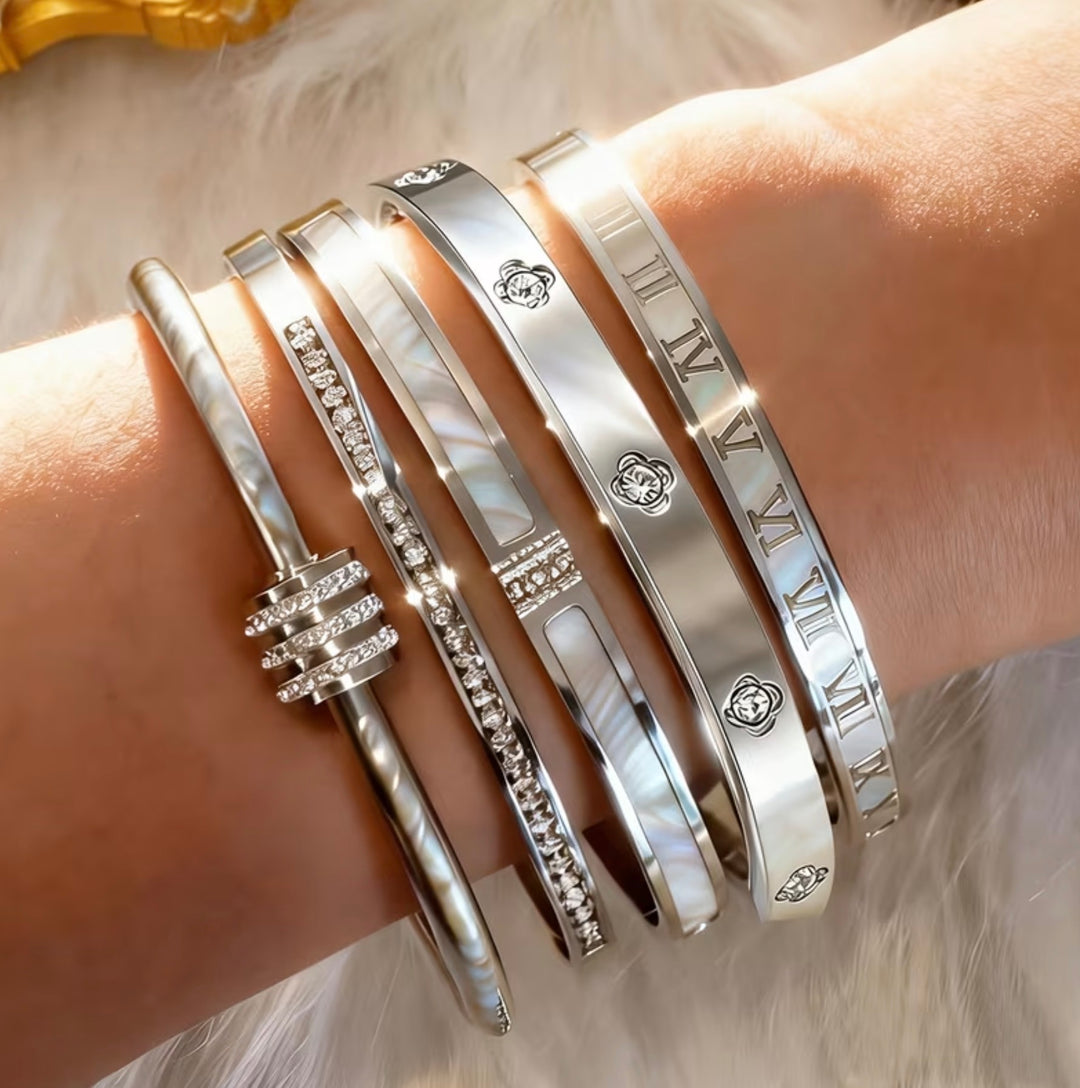 Five-piece silver-tone bangle bracelet set with crystal detailing, Roman numeral accents and clover design stacked on wrist.