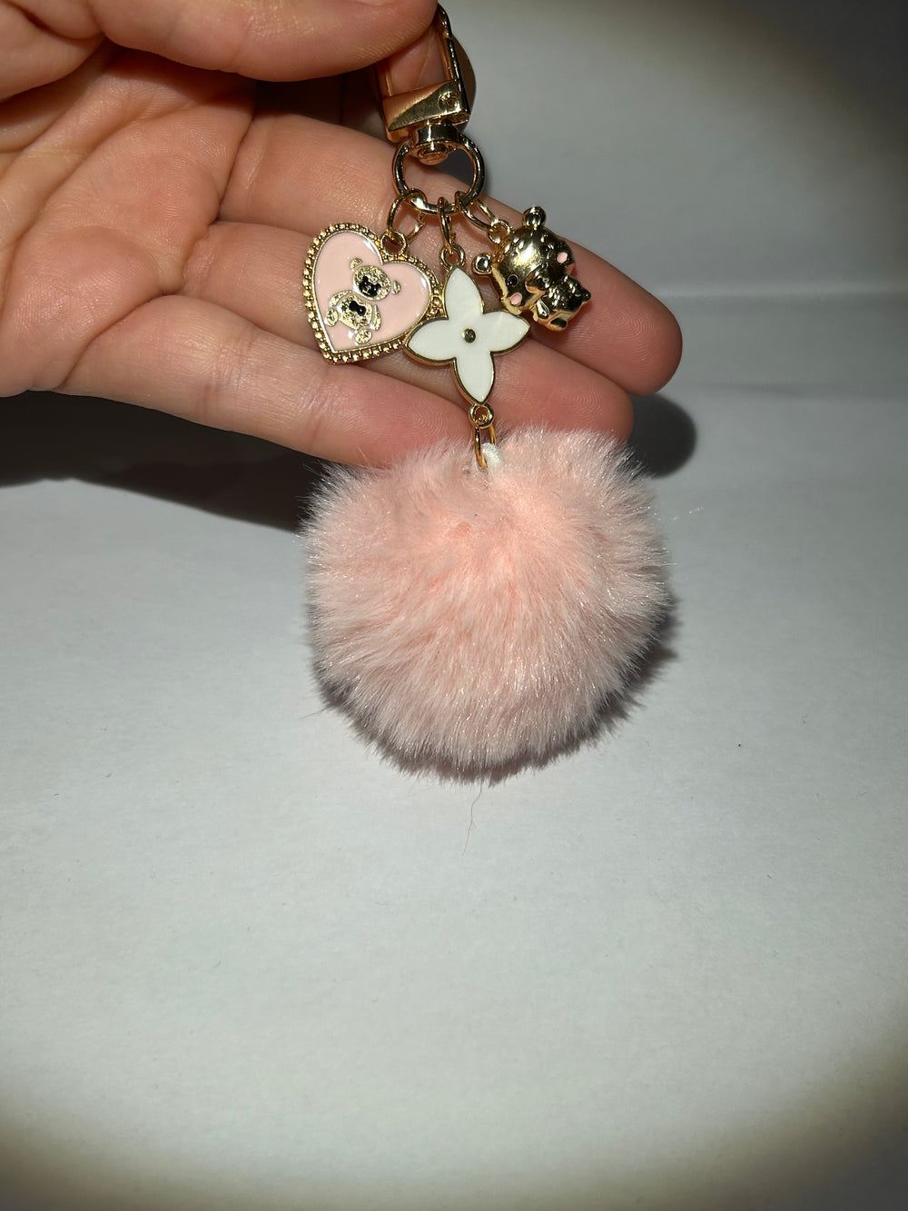A pink clover flower key ring with a fluffy pom-pom and additional charms attached to it.