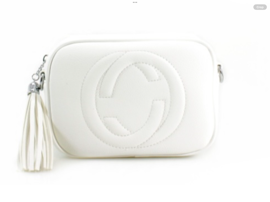 A white crossbody camera bag with embossed circle logo design, detachable strap and tassel zip detail