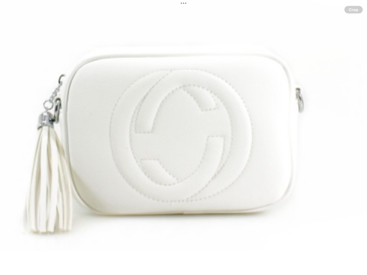 A white crossbody camera bag with embossed circle logo design, detachable strap and tassel zip detail