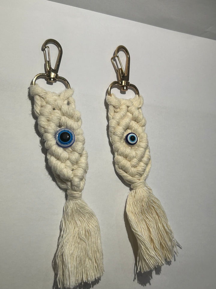 A pair of key rings with a blue eye design, made of a woven beige material