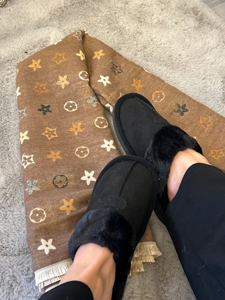 Black slip on slippers with neutral coloured flower detail on a beige/ brown scarf 