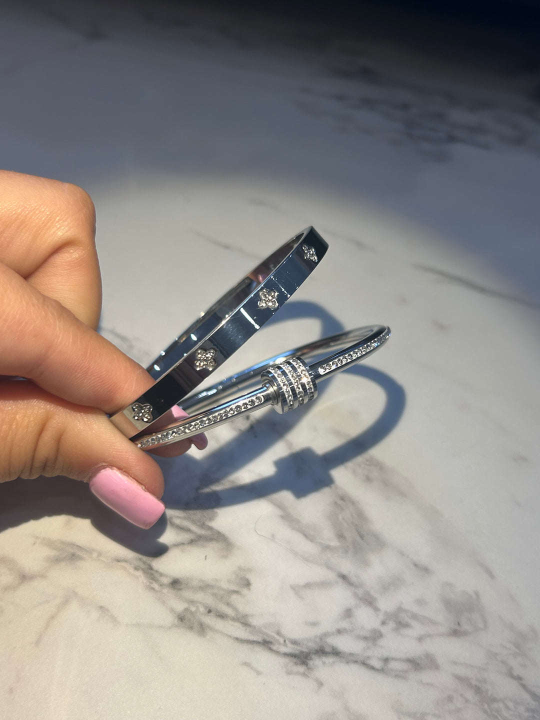 Two silver bracelets- one featuring screw-style detailing and the other with sparkling crystal embellishments and a wrap-around nail-inspired design.