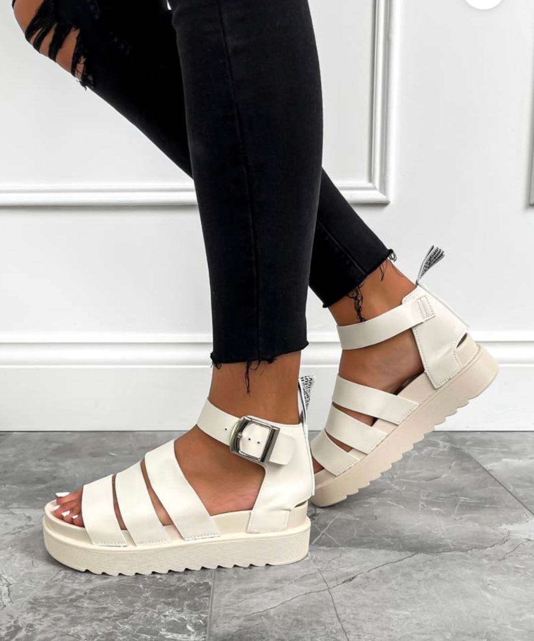 A pair of beige gladiator sandals with a buckle strap