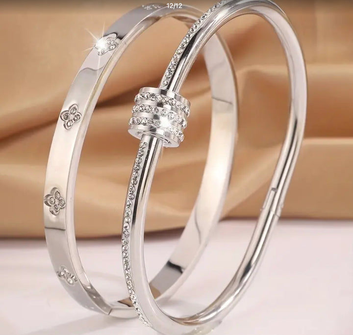 Two silver bracelets- one featuring screw-style detailing and the other with sparkling crystal embellishments and a wrap-around nail-inspired design.
