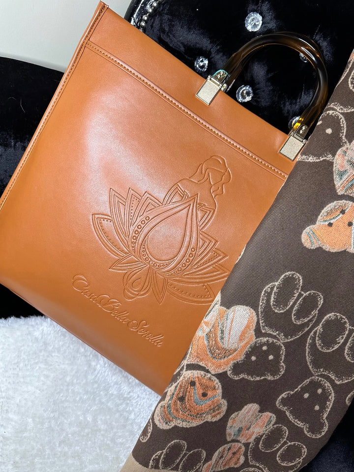 An image showing a tan handbag tote with an embossed cbs logo design, and a scarf. 