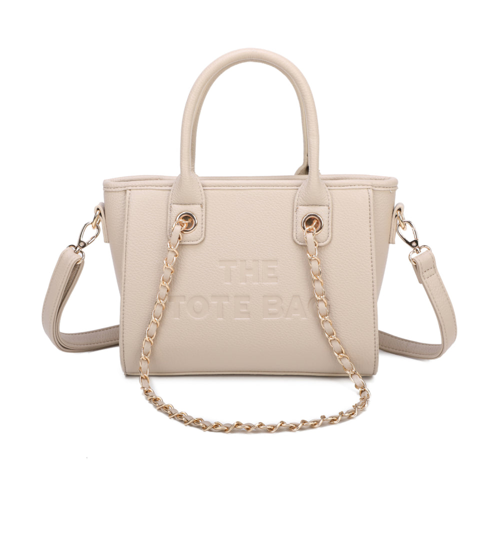 A beige tote bag with a chain handle, featuring a front zipper pocket and gold tone metal hardware. The 'THE TOTE BAG' is embossed on the front.
