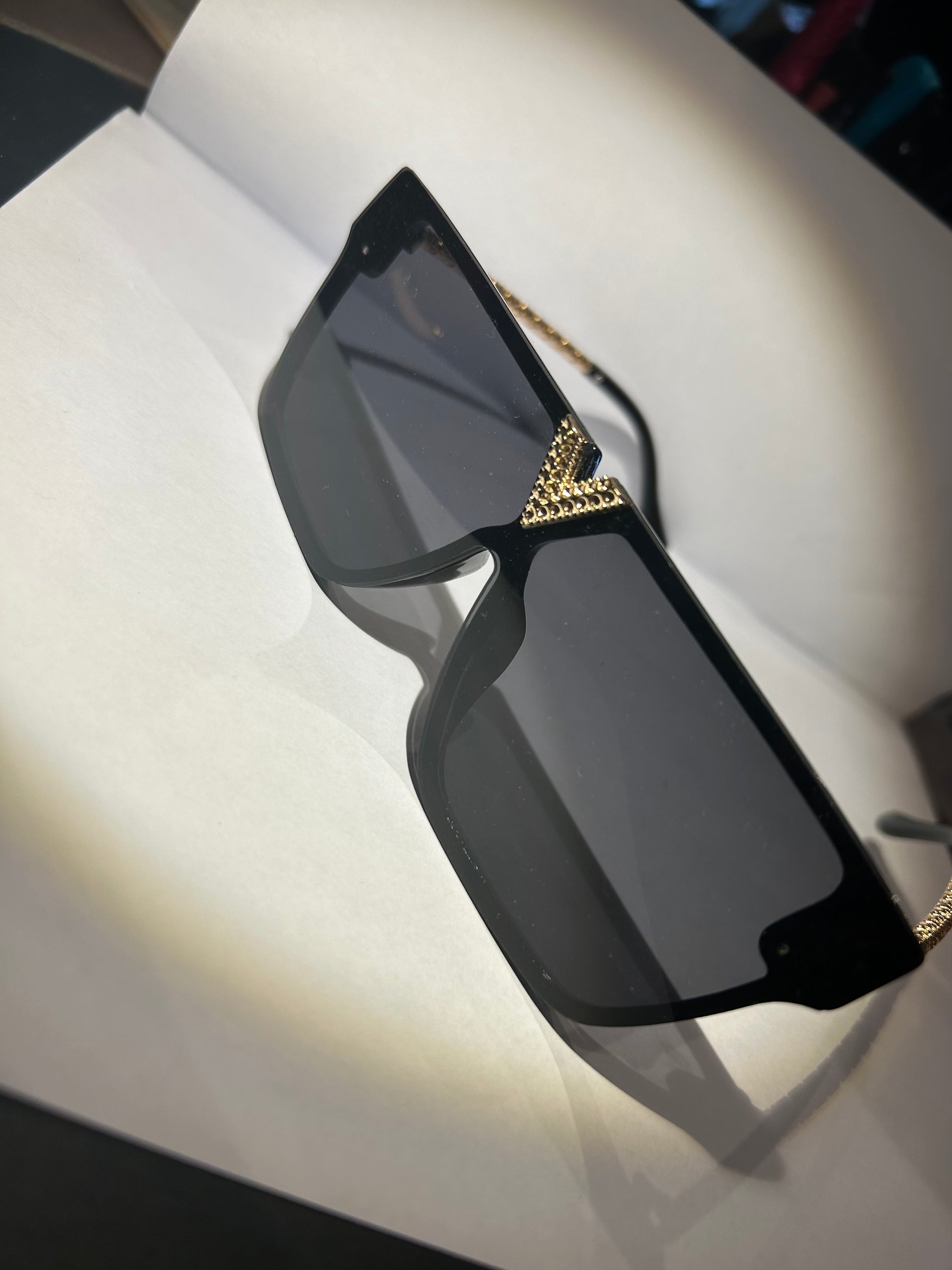 A pair of black sunglasses with gold detailing on the arms.