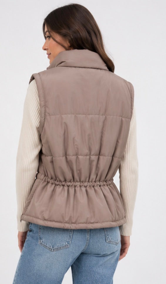 Taupe sleeveless padded gilet with high neck, quilted puffer finish, front popper fastening, buckle pocket detail and fitted waist