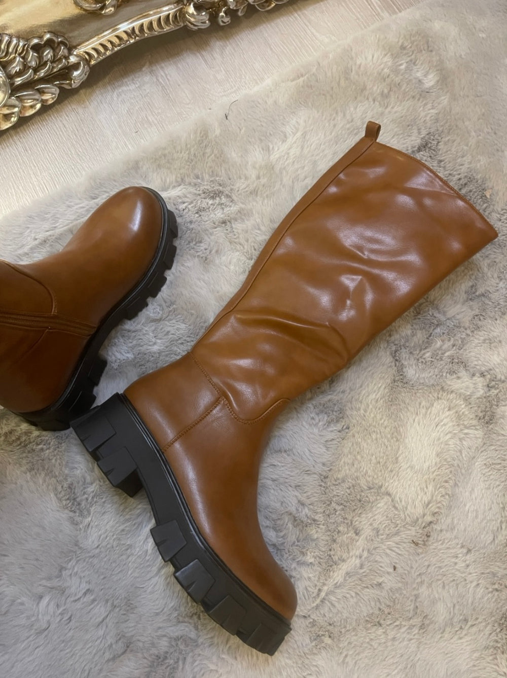 Tan knee high boots with black sole worn on feet, stylish women’s autumn footwear