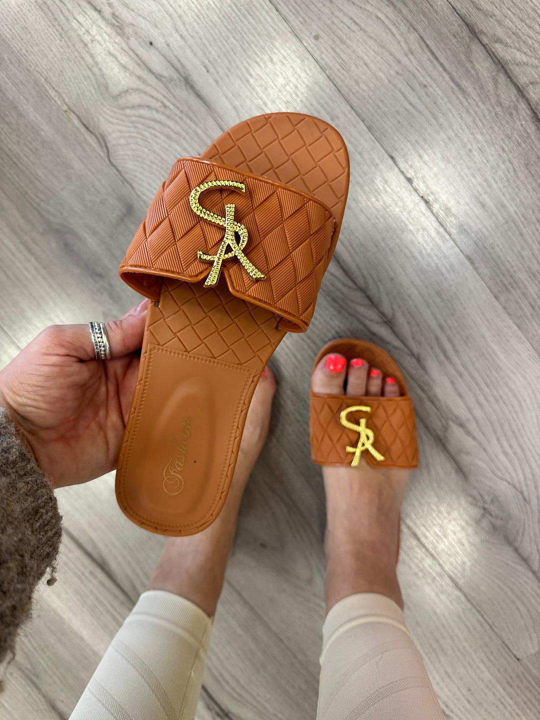 Tan  jelly sliders with gold letter details on them.