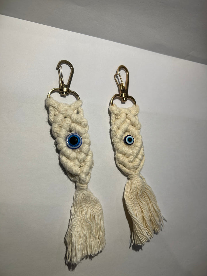 A pair of key rings with a blue eye design, made of a woven beige material