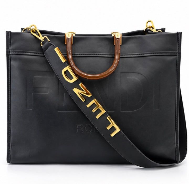Large black embossed tote bag with brown handles, gold hardware and wide statement shoulder strap