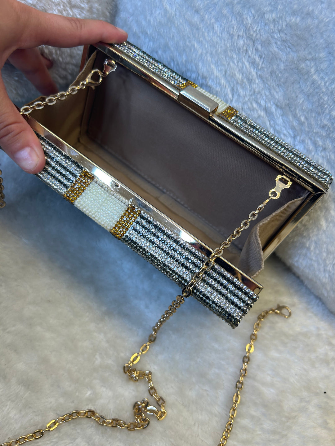 Decorative clutch bag with a chain strap held by a hand on a textured surface.