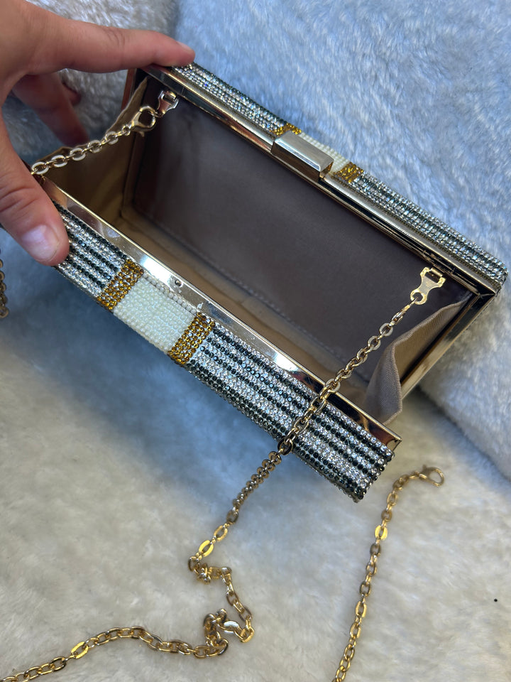 Decorative clutch bag with a chain strap held by a hand on a textured surface.