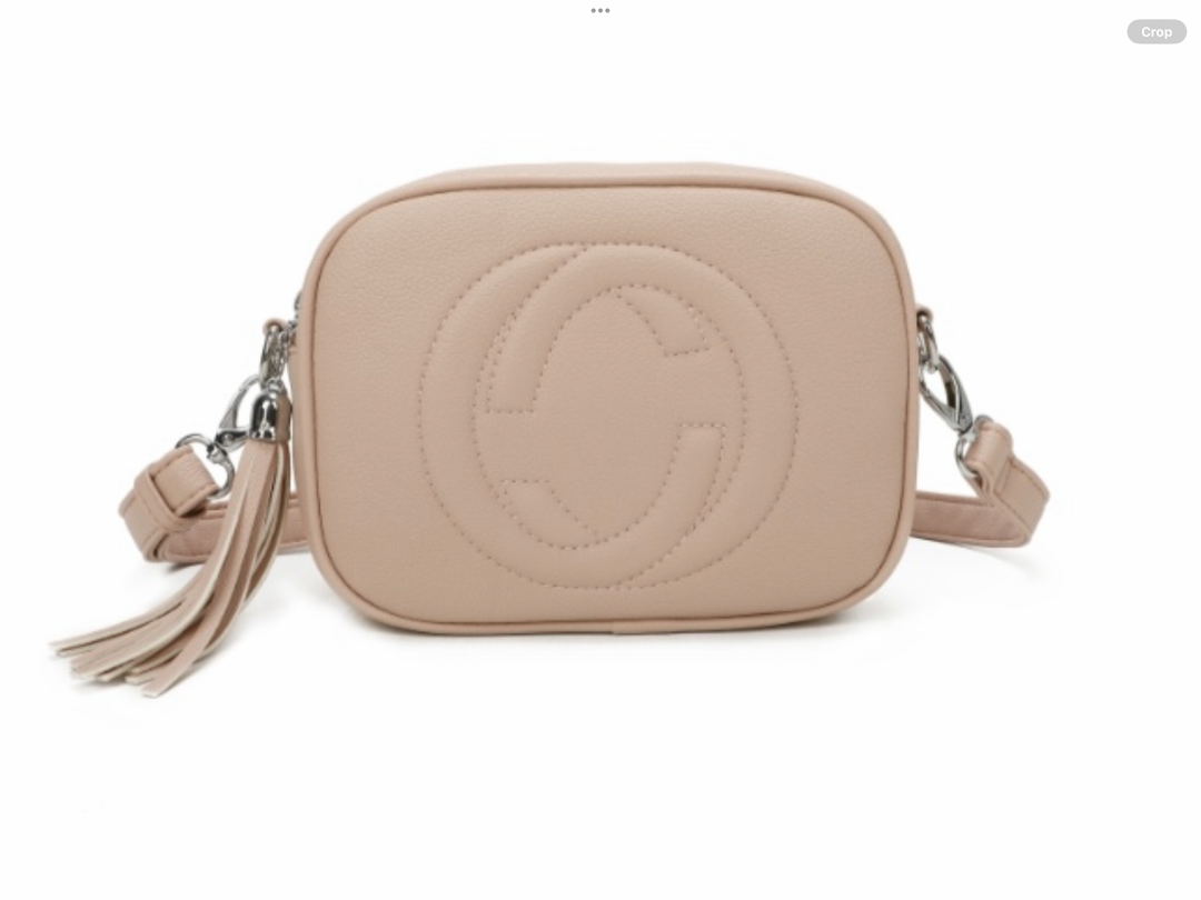 A pink crossbody camera bag with embossed circle logo design, detachable strap and tassel zip detail