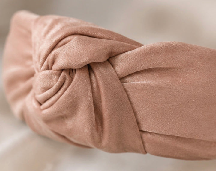 Soft pink satin knotted padded headband with elegant knot detail and comfortable design.