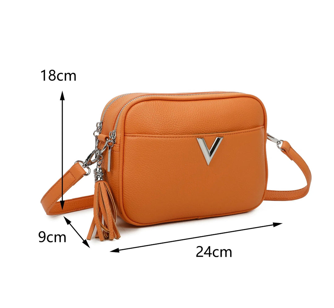 A orange faux leather crossbody bag with a double zip closure, silver tone metal hardware, and an adjustable long strap. It features a front pocket,