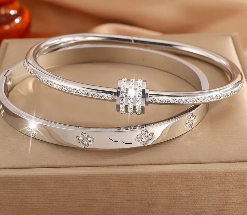 Two silver bracelets- one featuring screw-style detailing and the other with sparkling crystal embellishments and a wrap-around nail-inspired design.
