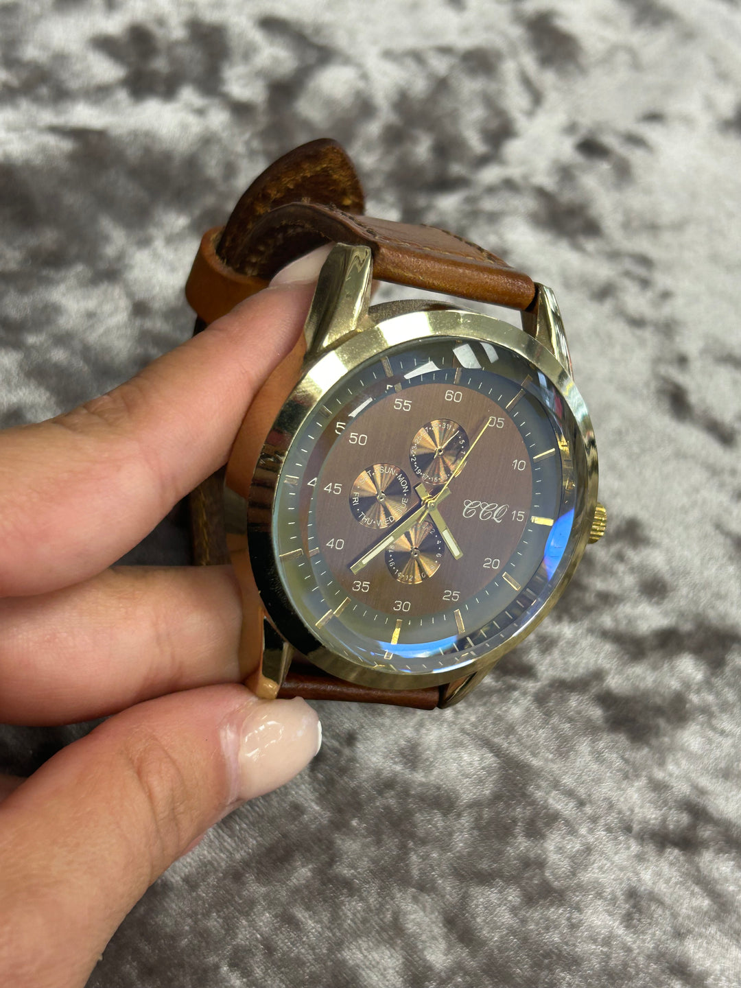 Gold watch with brown leather strap held by a hand on a textured gray background