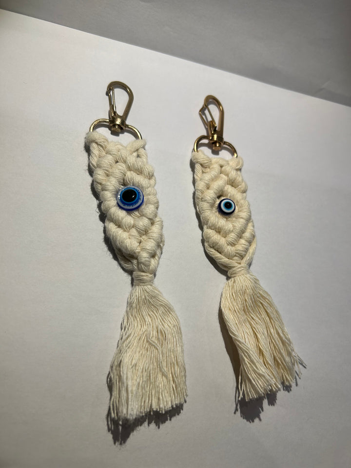 A pair of key rings with a blue eye design, made of a woven beige material