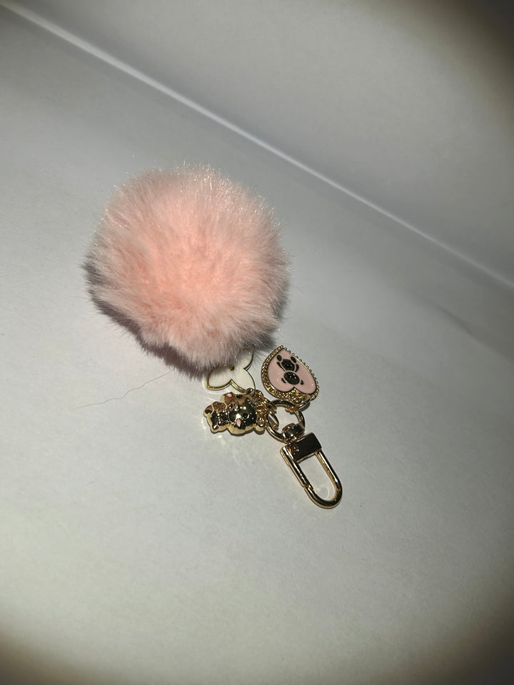 A pink clover flower key ring with a fluffy pom-pom and additional charms attached to it. back of charm