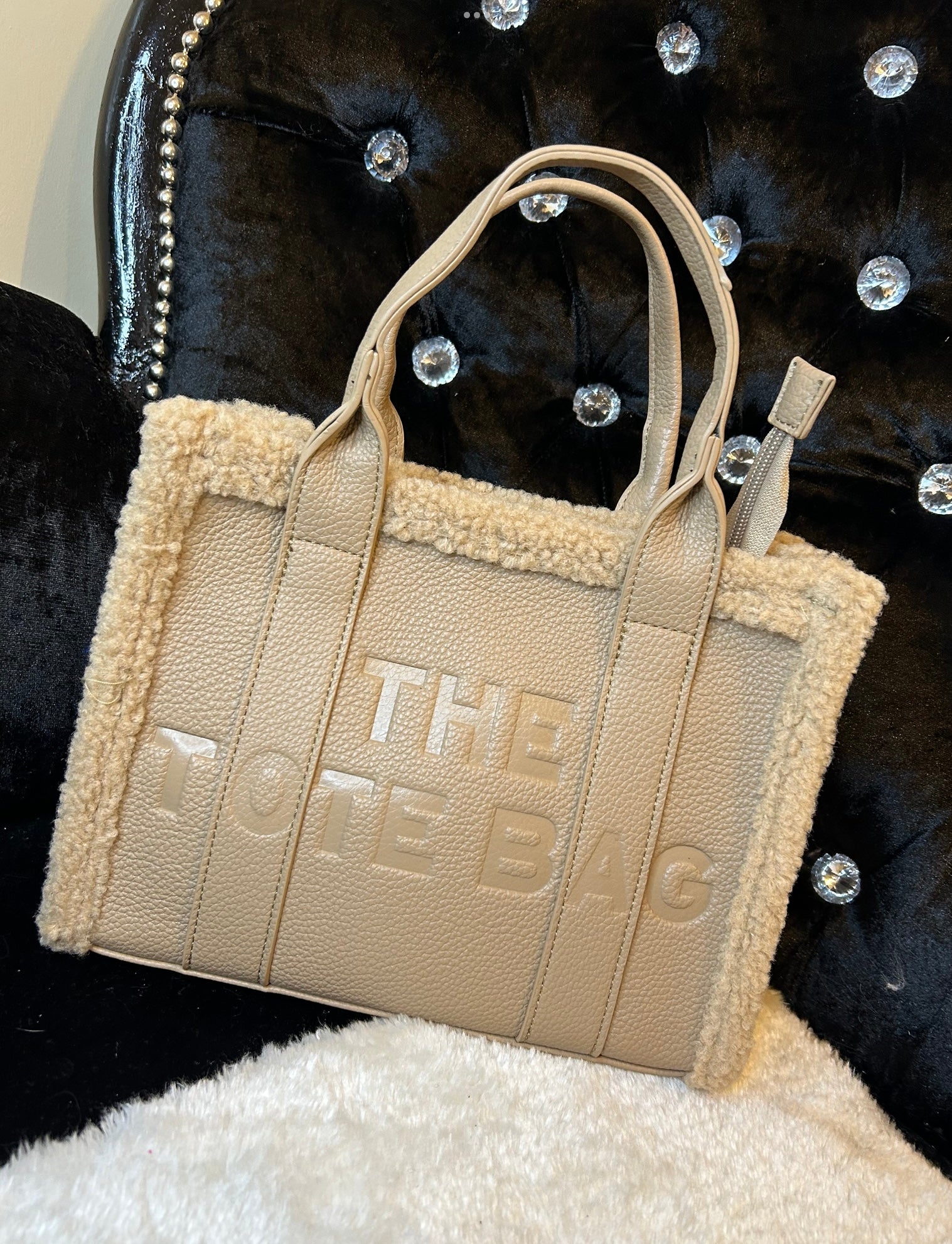 A beige mini tote handbag with debossed details and fuzzy edged trim, featuring an adjustable strap.