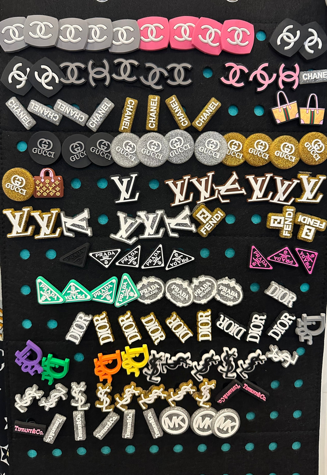 A variety of shoe charms displayed on a surface, including charms with letters, stars, and other shapes, some with a monochrome background.