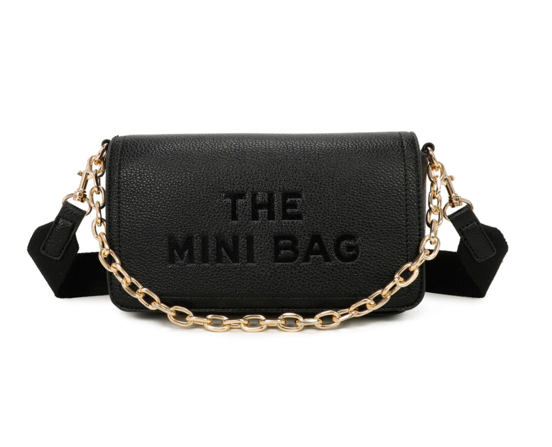 A black mini tote bag with a chain detail and the text 'THE MINI BAG' embossed on the flap. It includes a detachable across-the-body strap and gold tone metal hardware.
