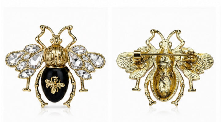 A gold-tone bee brooch shown from both front and back views on a white background. The front view features a black enamel abdomen and clear rhinestone wings, while the back view shows the pin&