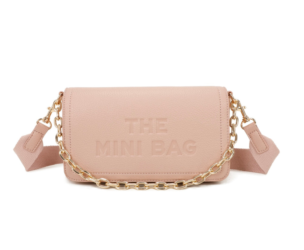 A pink mini tote bag with a chain detail and the text 'THE MINI BAG' embossed on the flap. It includes a detachable across-the-body strap and gold tone metal hardware.