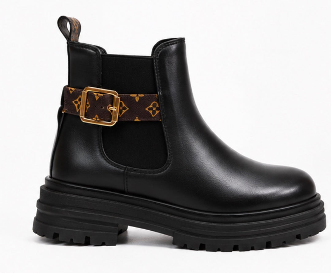 Black chunky Chelsea-style ankle boots with brown printed strap, gold buckle and cleated sole