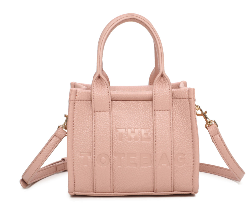 A pink mini tote bag with 'THE TOTE BAG' embossed on the front, featuring double grab handles and a detachable strap.