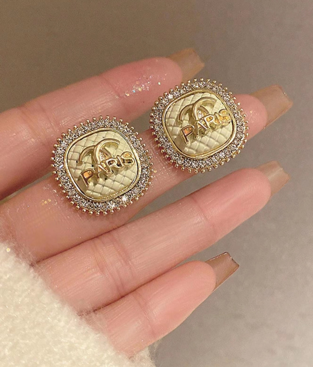 Gold and diamond-encrusted earrings held between fingers