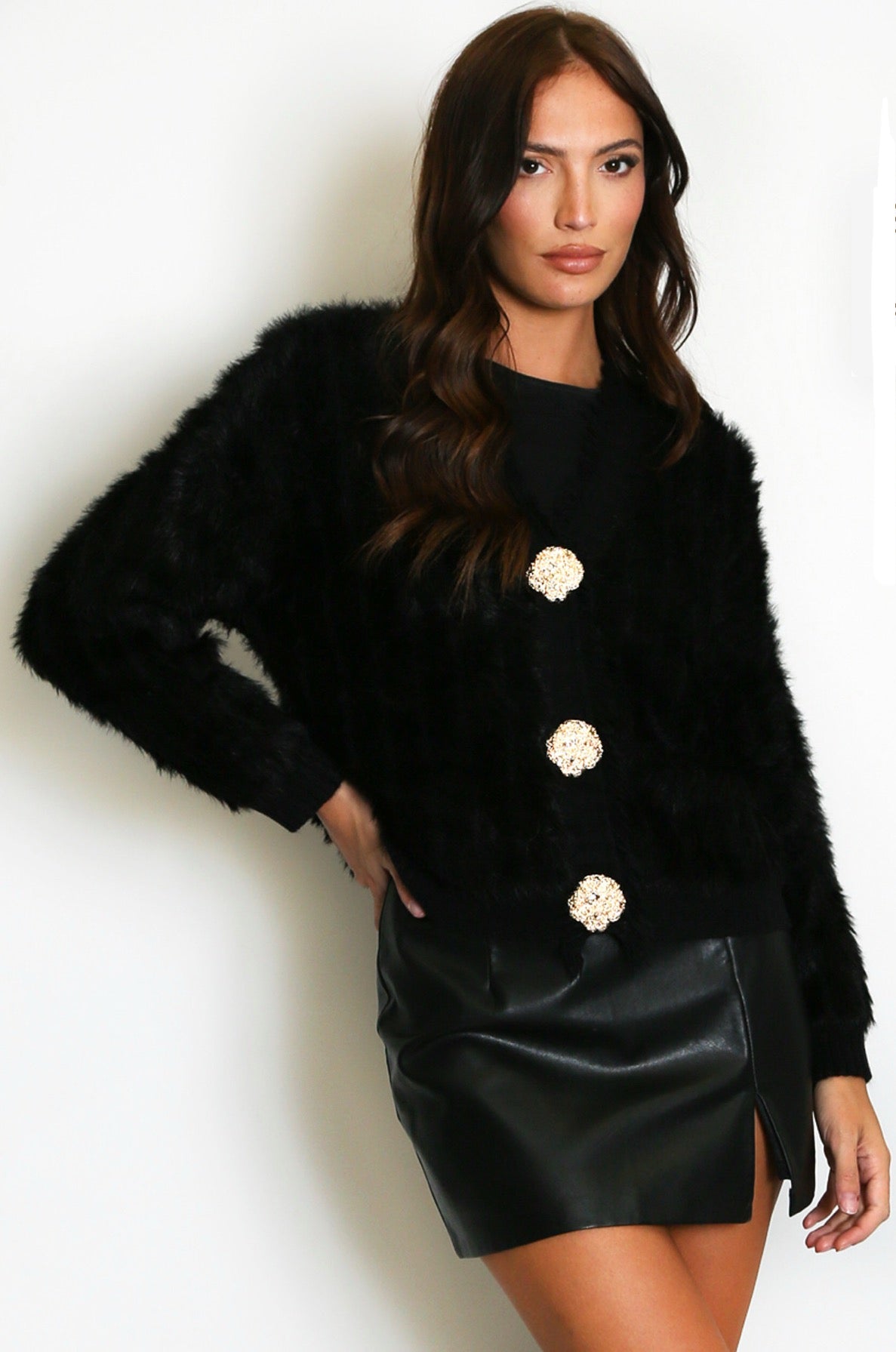 Woman wearing a black fur cardigan with gold buttons and a black leather skirt 