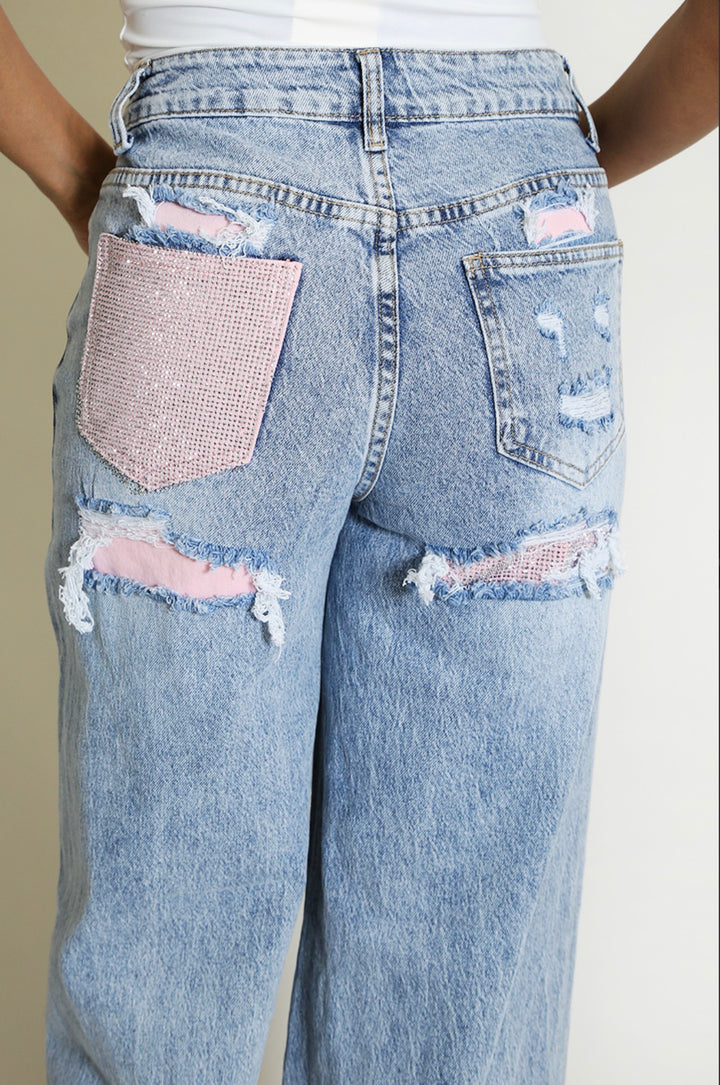     Close-up of distressed denim with pink underlay and rhinestone embellishmen