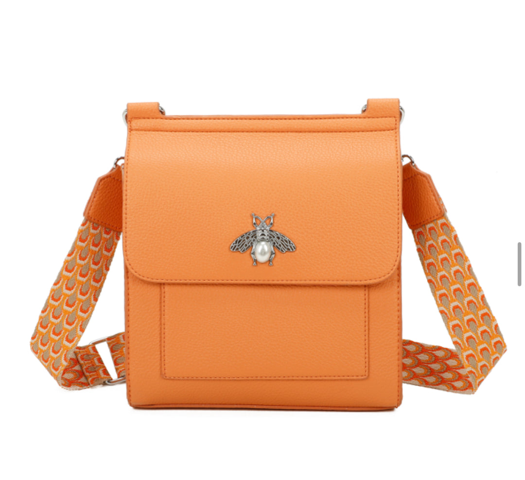 A orange satchel crossbody bag with a bee design on the front flap, featuring a camouflage pattern on the strap.