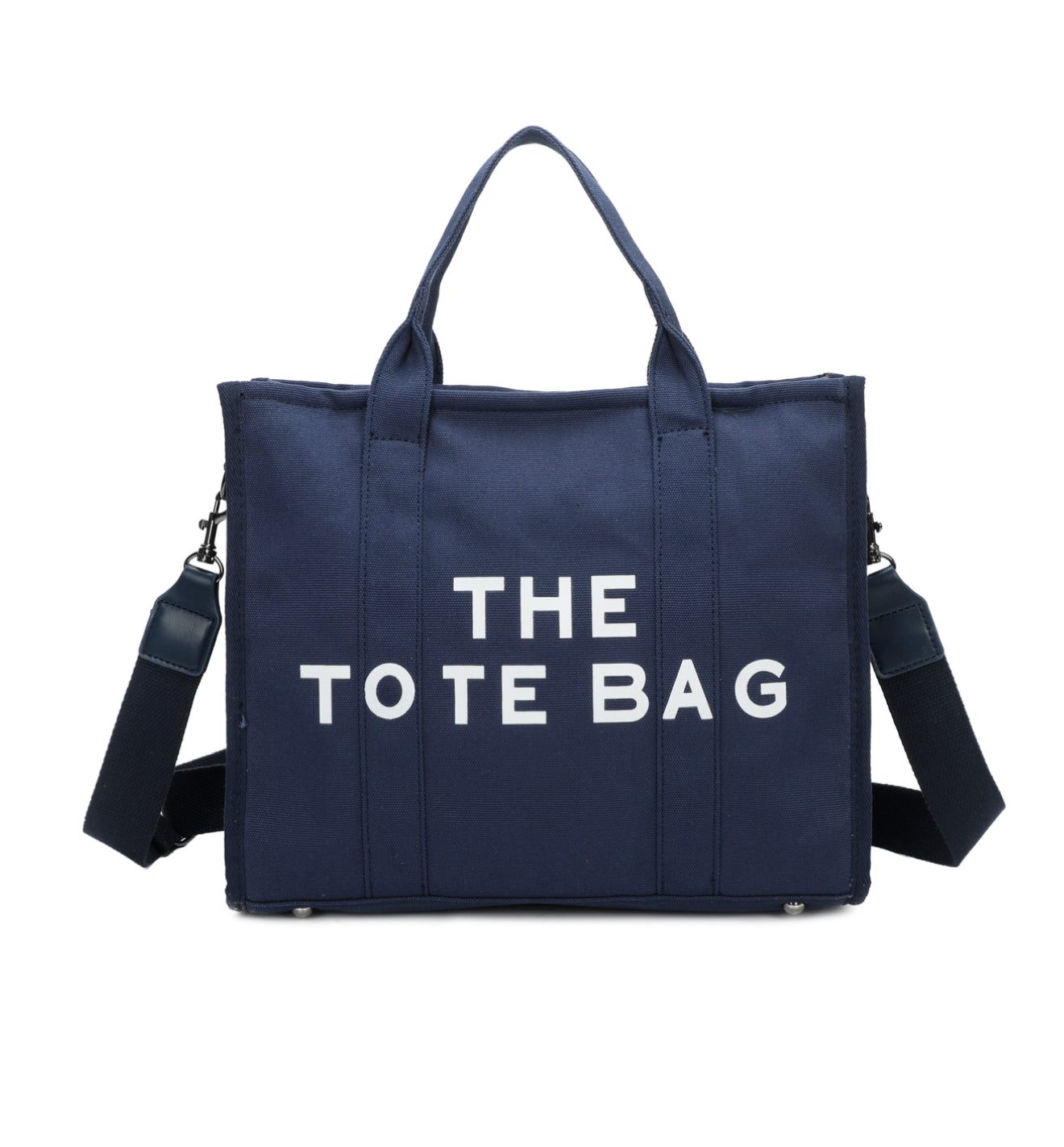 A navy canvas tote bag with 'THE TOTE BAG' printed in white text. It features double grab straps, a detachable and adjustable strap, and silver tone metal hardware