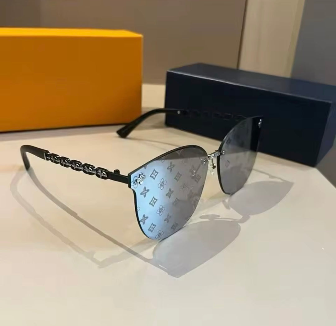 Luxury black rimless sunglasses with monogram style lenses and black chain detail arms displayed on a white surface.
