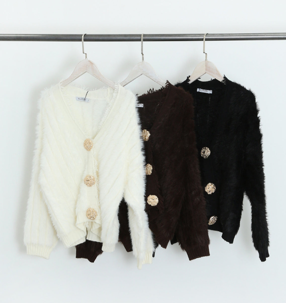 Three cardigans in white, brown, and black hanging on a rack.