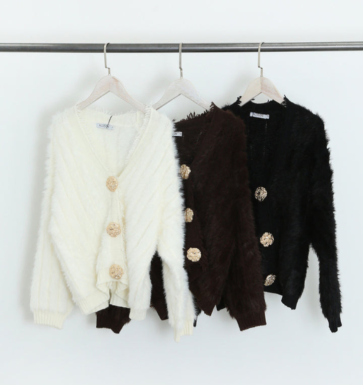 Three cardigans in white, brown, and black hanging on a rack.