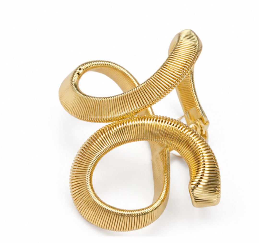 Gold sculptural twist cuff bangle bracelet with a textured finish displayed on a white background.