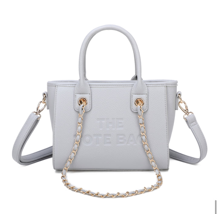 A grey tote bag with a chain handle, featuring a front zipper pocket and gold tone metal hardware. The &