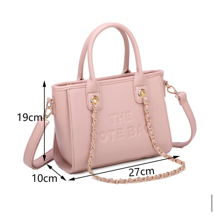 A pink tote bag with a chain handle, featuring a front zipper pocket and gold tone metal hardware. The &