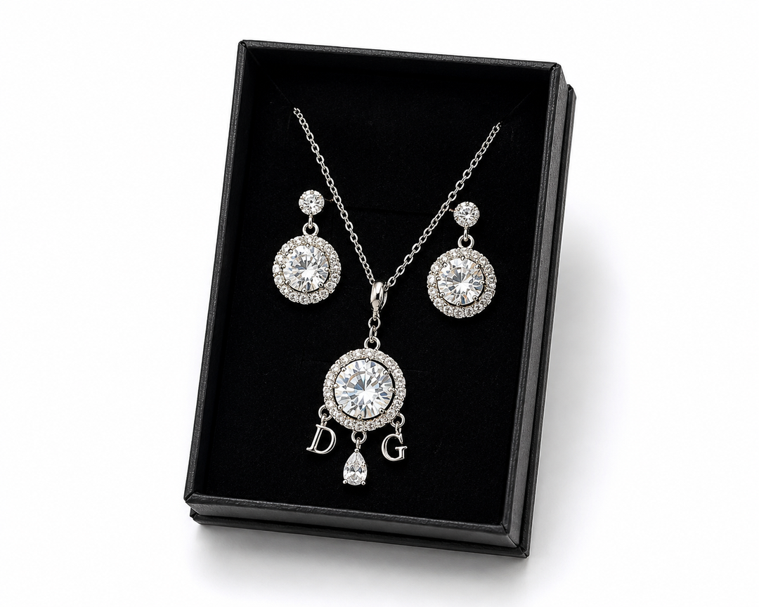 Silver crystal halo pendant necklace with decorative initial charms and matching halo drop earrings displayed in a black gift box.